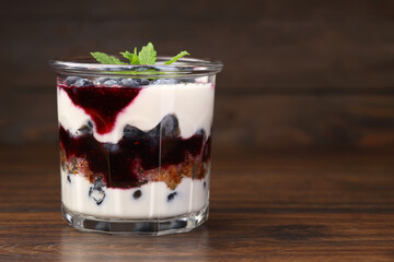 Tasty trifle dessert. Blueberries, sponge cake and whipped cream in glass on wooden table, space for text