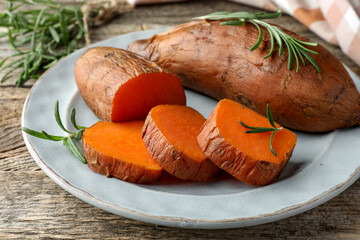 Tasty cooked sweet potatoes served with rosemary on wooden table, closeup
