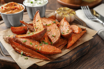 Tasty cooked sweet potatoes served with sauces on wooden table, closeup