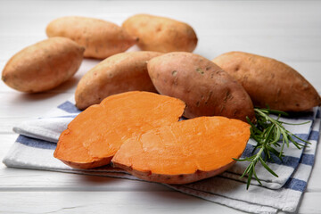 Fresh raw sweet potatoes and rosemary on white wooden table, closeup