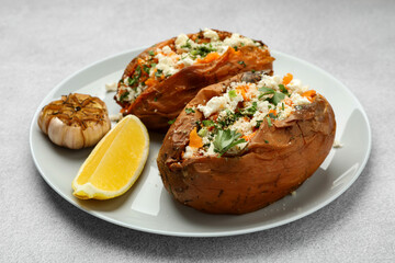 Tasty baked sweet potatoes with feta cheese, parsley and lemon slice on light textured table, closeup