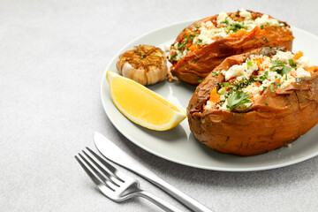Tasty baked sweet potatoes with feta cheese, parsley and lemon slice on light textured table, closeup. Space for text