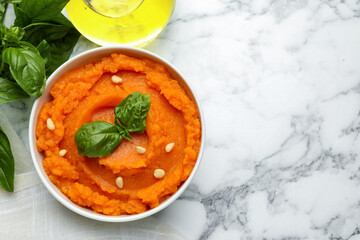 Tasty mashed sweet potato with basil and seeds in bowl on white marble table, flat lay. Space for text