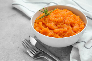 Tasty mashed sweet potato with rosemary in bowl served on grey textured table, closeup
