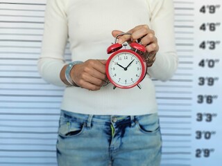 Woman in handcuffs holding alarm clock at police station