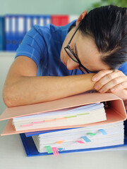 Overwhelmed office worker resting on files in a cluttered workspace