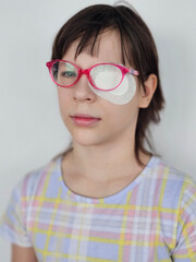 Fototapeta premium Girl wearing pink glasses with an eye patch, highlighting her focused expression at home concept