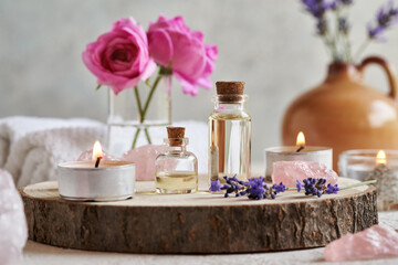 Essential oil bottles with lavender and pink rose flowers, rose quartz stones and white spa towels