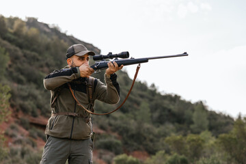 Hunter aiming with rifle in forest during hunt