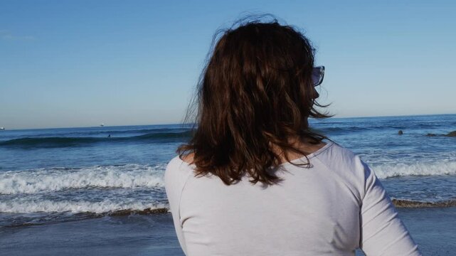 Mujer frente al mar con la mano en la cara mira a su alrededor y se va.