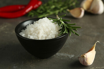 Sea salt in bowl, rosemary and garlic on grey table, closeup