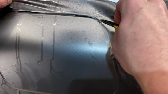 A specialist in wrapping a car with gray matte vinyl or ppf film in the process of work. Car wrapping specialists cover the car with gray matte vinyl film. Gray matte vinyl foil. Selective focus.
