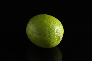 One fresh lime on black mirror surface, closeup