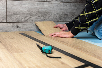 Worker installing laminate flooring in apartment under renovation.