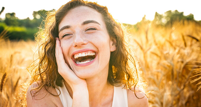 Happy beautiful woman smiling at camera in a wheat field - Delightful female enjoying summertime sunny day outside - Wellbeing, mental health, body care and happiness concept