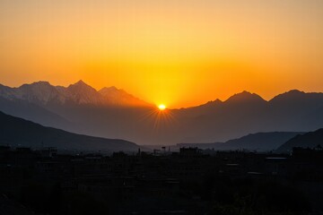 The sun is setting behind the mountains, casting a warm glow over the city below