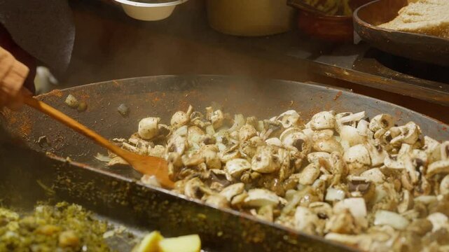 Frying Champignon Mushrooms with Vegetable Seasoning in a very big Pan on a stove with wooden spoon. Cooking cut mushrooms - fried champignon in a big frying pan