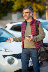 Man with car key and phone standing near parked cars