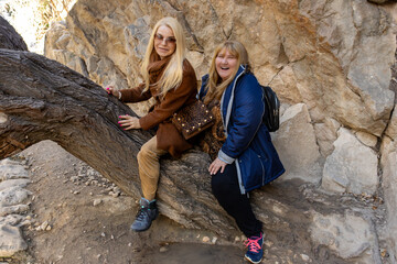 Two Smiling Women Posing on Tree Trunk Against Rocky Background