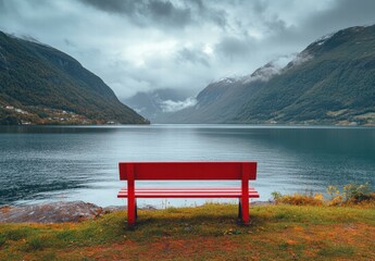 A red bench sits on a grassy hill overlooking a lake