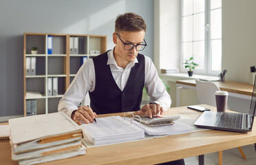 Young confident business man accountant working with financial documents sitting at the desk in...