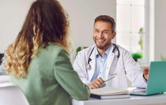 Conversation with doctor. Portrait of friendly male doctor happily listening to his female patient in medical office. Medic looks at woman in front of him. Concept of medicine, healthcare and people. - Powered by Adobe