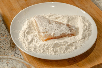 Piece of fish lies in flour before frying. Close-up