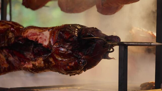Roasted a whole big pig on fire. Grilled on a big skewer. Roasting piglet on a spit turns slowly roasting it. Barbecue. Street food. 4k. Lechon or Suckling popular dish. pigs roasting on fire pit and 