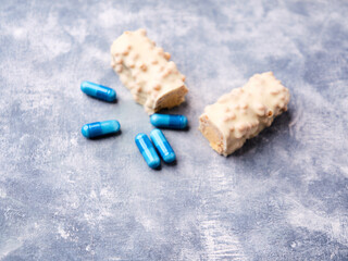 Protein bar in two pieces and amino acids capsules on wooden background. Soft focus. Close up. Copy space