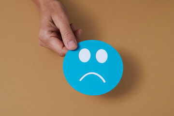 man holds a blue paper sad face in his hand