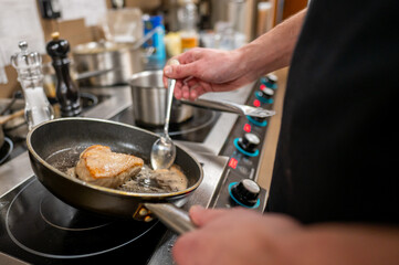 A chef skillfully cooks a piece of meat in a frying pan on a modern stovetop, using a spoon to...