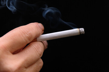 Cigarette allumée en main en gros plan sur fond noir