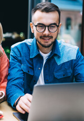 Positive caucasian male and female watching video on laptop computer co operating on project,20s...