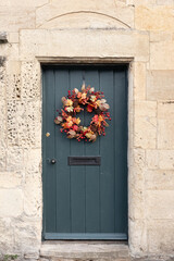 Old wooden door entrance to cottage made from limestone with autumn coloured foliage wreath