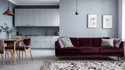 A stylish Scandinavian loft with light gray walls, a burgundy velvet sofa, and a geometric patterned rug. The kitchen area has sleek white cabinets and a wooden dining table with modern chairs.