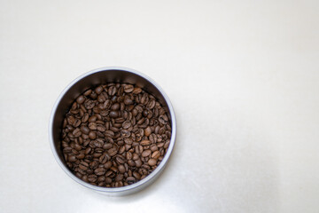 Top View of a Metal Container Filled with Roasted Coffee Beans on a Neutral Background