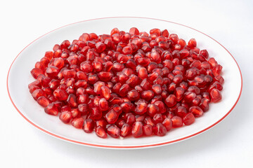 Gennevilliers, France - 01 02 2024: Close up of a white plate filled with red triangular pomegranate seeds on a white background.