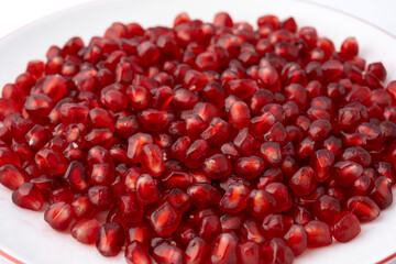 Gennevilliers, France - 01 02 2024: Close up of a white plate filled with red triangular pomegranate seeds on a white background.