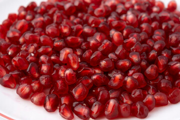 Gennevilliers, France - 01 02 2024: Close up of a white plate filled with red triangular pomegranate seeds on a white background.