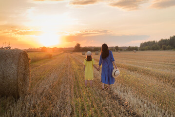 Beautiful Mother and Daughter in a Field with Haystacks at Sunset, Wearing Blue and Yellow Dresses Inspired by the Ukrainian Flag