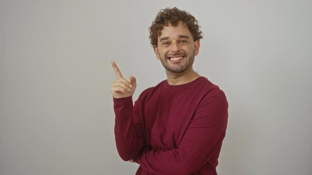 Young hispanic man standing and wearing t-shirt, pointing one finger up with a bright idea and happy expression, emulating success over isolated white background