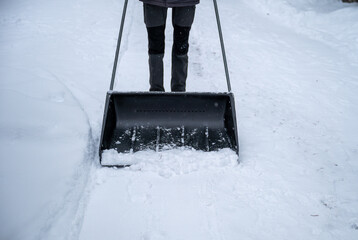 person clearing snow with a large snow shovel on a snowy pathway. concept of outdoor chores
