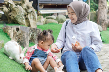 A joyful moment between an asian mother and her daughter feeding a cute rabbit outdoors.