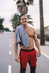 Obraz premium Half length portrait of successful sportsman with shirtless smiling at camera during workout time for training muscles, pumped up athlete with perfect body shape posing ready for physical warm up