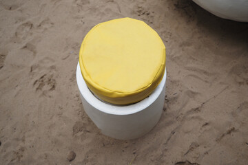 Unique modern stool with yellow top rests on sand in artistic outdoor setting.