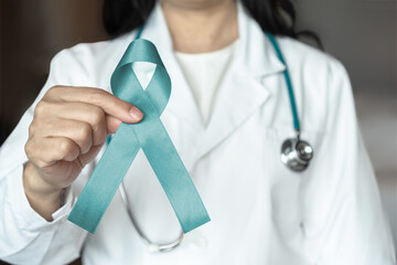 Teal awareness ribbon in female doctor's hand, bow color for supporting patient with Ovarian...