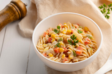 Homemade macaroni salad with trivelle pasta and canned tuna, carrot, Green Pea, corn and mayonnaise dressing in a white plate on wooden table.