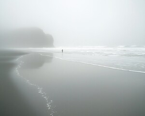 Solitary figure walking on a foggy beach.