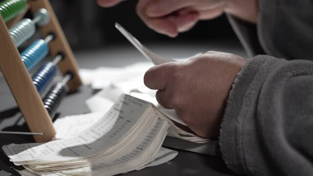 A man is counting expenses on wooden accounts. The man is keeping records. Wooden abacus instead of a calculator.