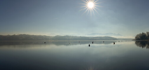 Der Simssee in Bayern im Winter mit Nebel Sonne und Spiegelung der Landschaft 
